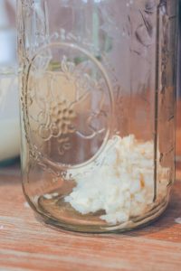 a half gallon glass jar with kefir grains at the bottom sitting on a table